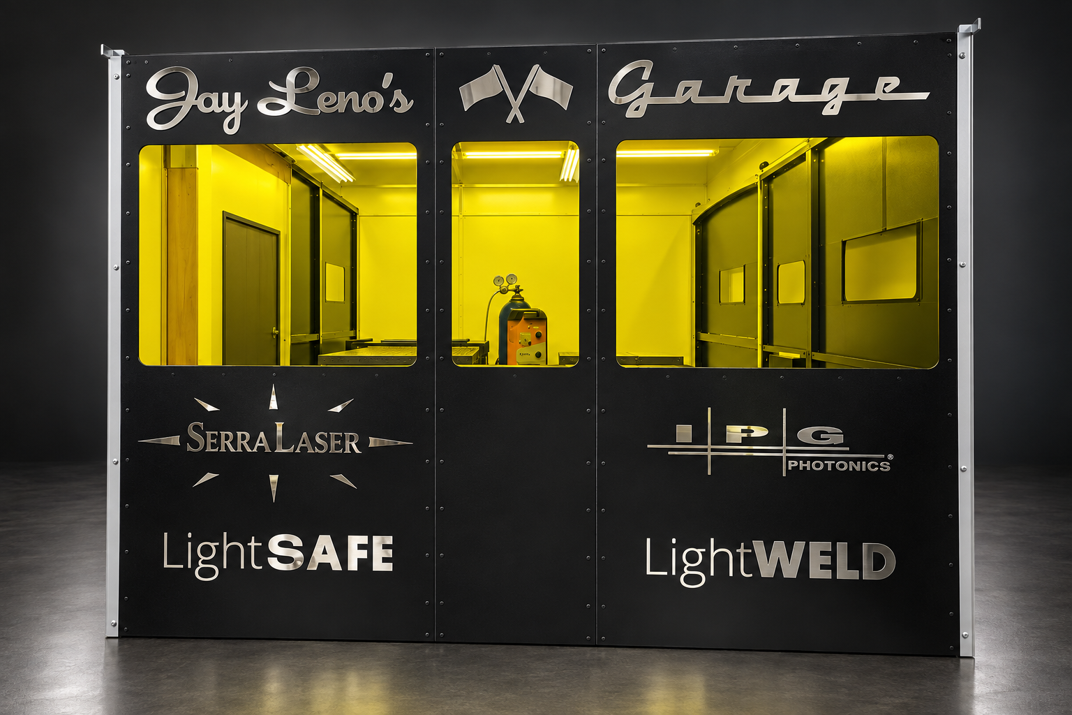 A custom 10 × 10 ft, three-wall LightSAFE system for Jay Leno’s Garage, featuring signature metallic branding and large laser viewing windows.